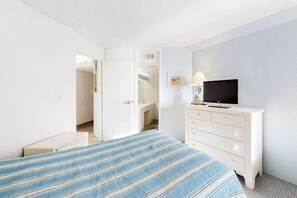 A hotel room with a bed, a TV on a dresser, and a door leading to a bathroom. - Oceanfront Condo with a Balcony, Beach Views, AC, WiFi & Shared Outdoor Pool (Ocean City)