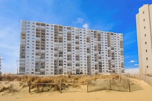 A multi-story hotel with balconies, a sandy beach in the foreground, and a clear sky. - Plaza 1307 (Ocean City)