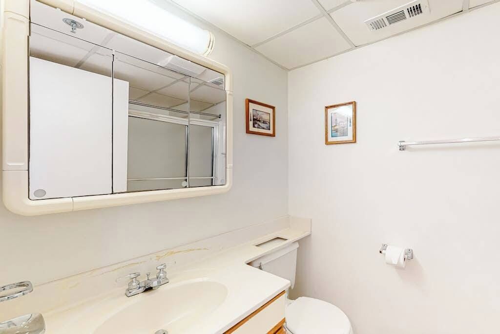 A bathroom with a sink, mirror, toilet, towel rack, and two framed pictures on the wall.