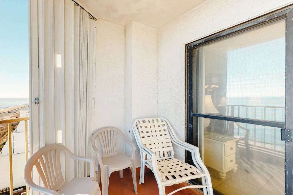 Ein Balkon mit zwei weißen Plastikstühlen, einer Glastür und Blick auf das Meer.