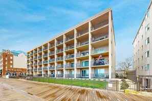 A multi-story hotel with balconies, a wooden boardwalk, and a sign for 'The Dough Roller.' - Oceanfront condo on the boardwalk with balcony, central AC, WiFi, & great view (Ocean City)