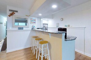 A kitchen with white cabinetry, a granite countertop, and three wooden stools. - Oceanfront condo on the boardwalk with balcony, central AC, WiFi, & great view (Ocean City)