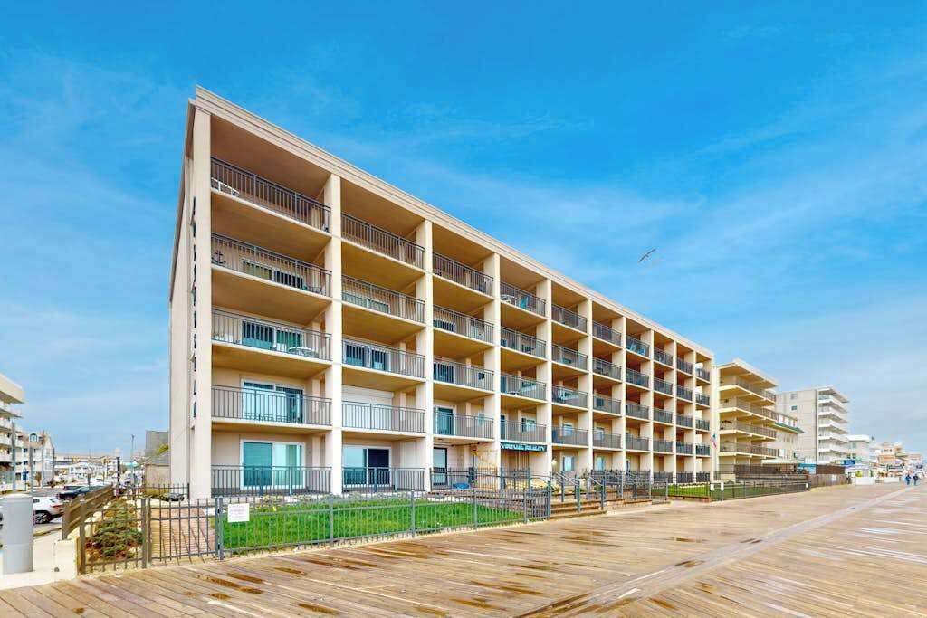 Een hotel met meerdere verdiepingen, balkons, een houten boardwalk en een helderblauwe lucht.