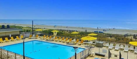 A swimming pool with sun loungers and umbrellas, a view of the beach, and a clear sky.