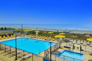 A swimming pool with sun loungers and umbrellas, a view of the beach, and a clear sky. - Plaza 1511 (Ocean City)