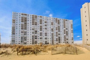 A multi-story hotel with a uniform facade, located near a sandy beach with a wooden fence. - Plaza 1511 (Ocean City)