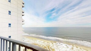 Un edificio alto con un balcone che si affaccia su una spiaggia sotto un cielo sereno.