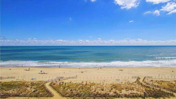 Una spiaggia con cielo sereno, una riva sabbiosa e alcune persone.