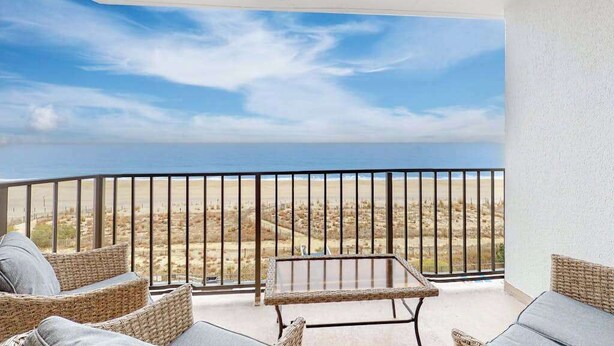 Un balcone con mobili in vimini, un tavolo in metallo e vista sull'oceano e sul paesaggio desertico.