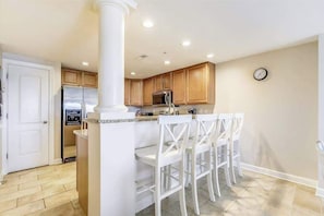 Una cocina con armarios de madera, un refrigerador de acero inoxidable y taburetes blancos.
