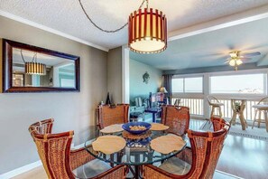 A dining area with a round glass table, wicker chairs, a hanging light fixture, and a ceiling fan. - Our Place At The Beach 206B (Ocean City)