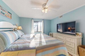 A bedroom with a bed, a television, a ceiling fan, and a window. - Our Place At The Beach 206B (Ocean City)