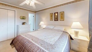 Ein Schlafzimmer mit einem Bett, Nachttischlampen, einem Deckenventilator und gerahmten Bildern an der Wand.