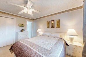 Ein Schlafzimmer mit einem Bett, Nachttischlampen, einem Deckenventilator und gerahmten Bildern an der Wand.