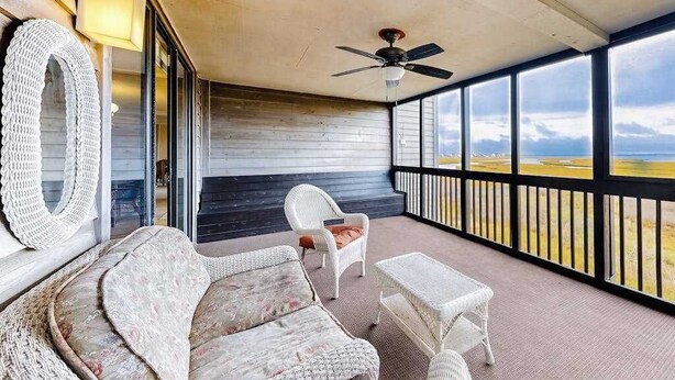 Eine überdachte Veranda mit Korbmöbeln, einem Deckenventilator und Blick auf die Landschaft.