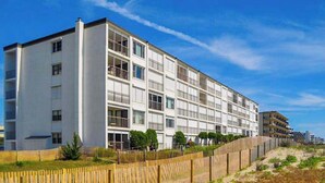 Un immeuble à plusieurs étages doté de balcons, une plage de sable au premier plan et un ciel dégagé.