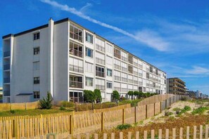 A multi-story building with balconies, a sandy beach in the foreground, and a clear sky. - Oceanfront Condo w/ Balcony, Sunrise Views, WiFi, AC & Washer/Dryer (Ocean City)