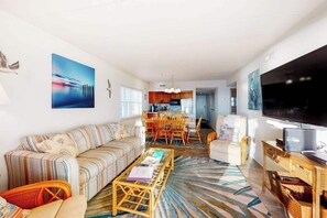 A modern living room with a sofa, coffee table, TV, and artwork. - Oceanfront Condo w/ Balcony, Sunrise Views, WiFi, AC & Washer/Dryer (Ocean City)
