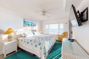 A bedroom with a bed, a ceiling fan, a TV, a window with blinds, and a chair. - Oceanfront Condo w/ Balcony, Sunrise Views, WiFi, AC & Washer/Dryer (Ocean City)