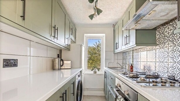 A compact kitchen with a washing machine, a stove, and a window with a view of trees. - Modern 2-Bed Apartment in Reading (Berkshire)