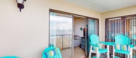 A balcony with turquoise chairs, a glass door leading to an interior room, and a wall-mounted light fixture.