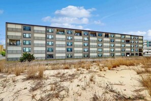 A multi-story building with balconies, located near a sandy area with sparse vegetation. - Ocean Trail 503 (Ocean City)