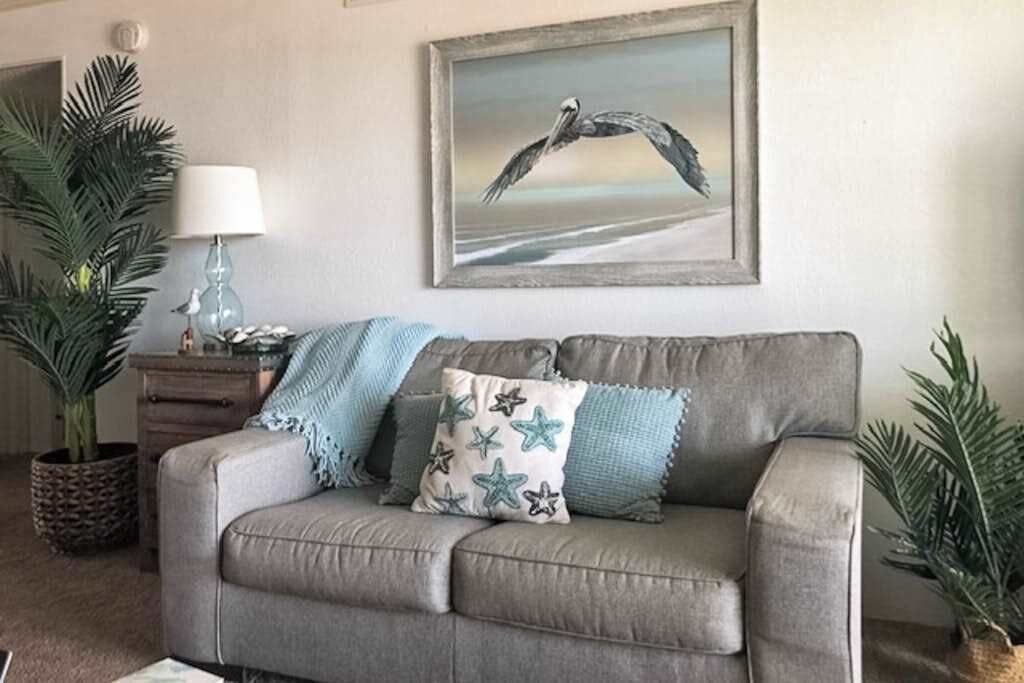 Ein graues Sofa mit Kissen in Sternenmuster, ein gerahmtes Meeresbild und eine Lampe auf einem Holznachttisch.