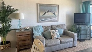 Ein Wohnzimmer mit einer Couch, einem Fernseher, einem gerahmten Bild und einer Lampe.