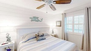 Ein Schlafzimmer mit einem Bett, einem Deckenventilator, einem Fenster mit Vorhängen und einer Wanddekoration.