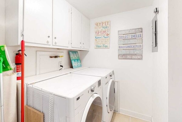 A laundry room with a washing machine, dryer, and a fire extinguisher. There are signs on the wall with summer rules. - Ocean Hideaway 511 (Ocean City)