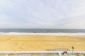 Blick auf einen Strand vom Balkon mit Geländer, einer Holzterrasse und einem Rettungsschwimmerstand.