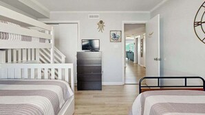 Een slaapkamer met stapelbedden, een dressoir, een televisie en een gang naar een andere kamer.