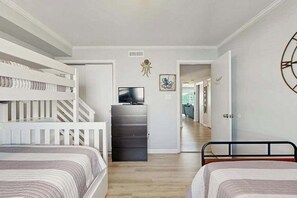 A bedroom with bunk beds, a dresser, a TV, and a hallway leading to another room. - Second-Floor Condo 1 Block from the Beach w/ Balcony, AC, WiFi & Shared Pool (Ocean City)