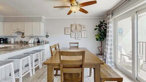 Een eethoek met een houten tafel, stoelen, een plafondventilator en een groot raam met uitzicht.