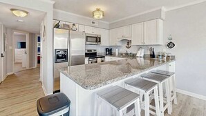 Een moderne keuken met witte kastjes, een granieten aanrechtblad en een centraal kookeiland met barkrukken.
