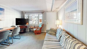 Una habitación con sofá, televisión, escritorio y una silla.