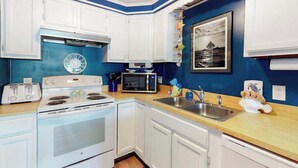 Una cocina con armarios blancos, estufa, microondas y pileta.