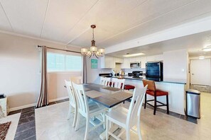 A modern kitchen with white cabinets, a dining table with chairs, and a chandelier. - Waterfront Family-Friendly Condo w/Private Balcony, A/C, Shared Outdoor Pool (Ocean City)