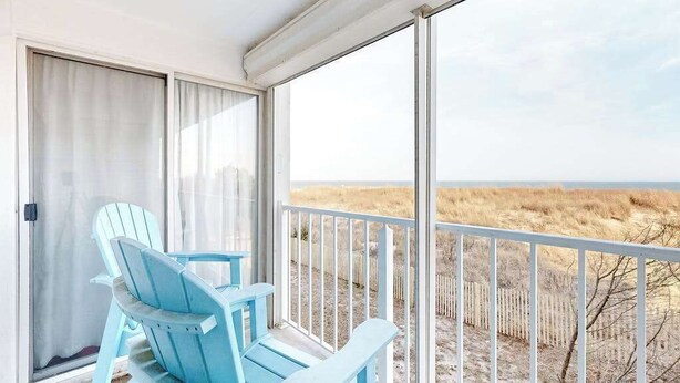 Uma varanda com vista para a praia, duas cadeiras Adirondack azuis e um corrimão branco.