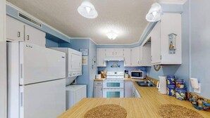 Eine kleine Küche mit weißen Geräten, einem Holztisch und einer blauen Wand.