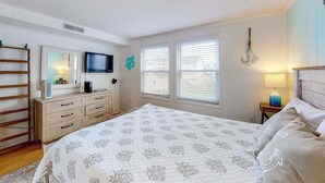 Ein Schlafzimmer mit Bett, Schminktisch, Fernseher, Fenstern und einer Chandelier.