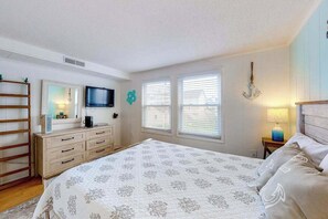 A bedroom with a bed, dresser, TV, windows, and a chandelier. - Budget-Friendly Beach Condo w/Private Washer/Dryer, Central A/C, WiFi (Ocean City)