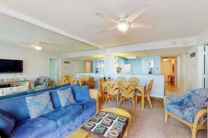 A living room with a sofa, coffee table, and dining area with chairs. - Breezy inviting condo with balcony, pools, gym, game room & tennis (Ocean City)