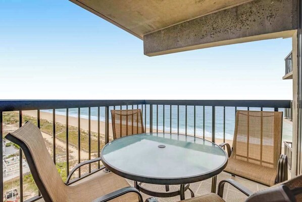 Un balcón con mesa y sillas de vidrio, con vista a la playa.