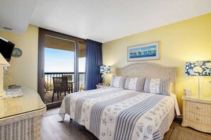Un dormitorio con cama, televisión, escritorio y balcón con vistas.