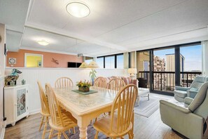 Un comedor con una mesa y sillas de madera, un armario blanco con objetos decorativos y un balcón con vistas a edificios.