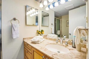 Un baño con lavamanos de mármol, dos espejos, un perchero y un florero con flores amarillas.