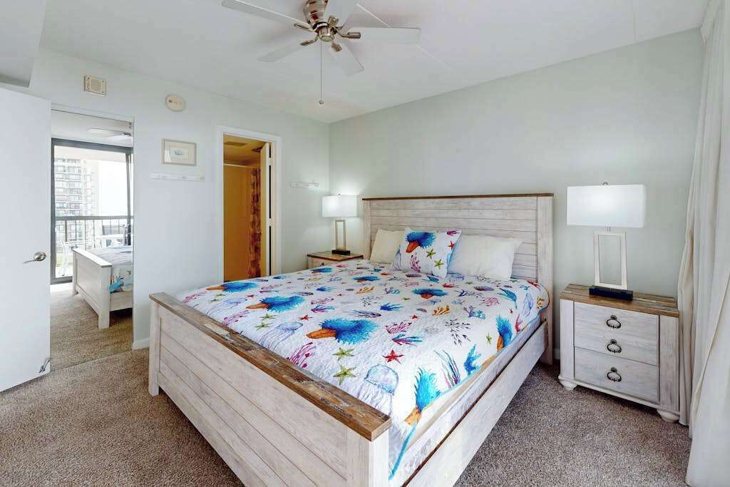 A bedroom with a bed, bedside tables, a ceiling fan, and a view through an open door.