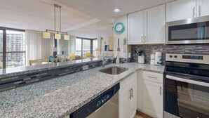 A modern kitchen with granite countertops, stainless steel appliances, and white cabinetry. - Bright, ocean-view condo with balcony, AC, pools, saunas & gym (Ocean City)