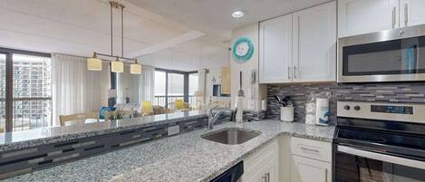 A modern kitchen with granite countertops, stainless steel appliances, and white cabinetry.